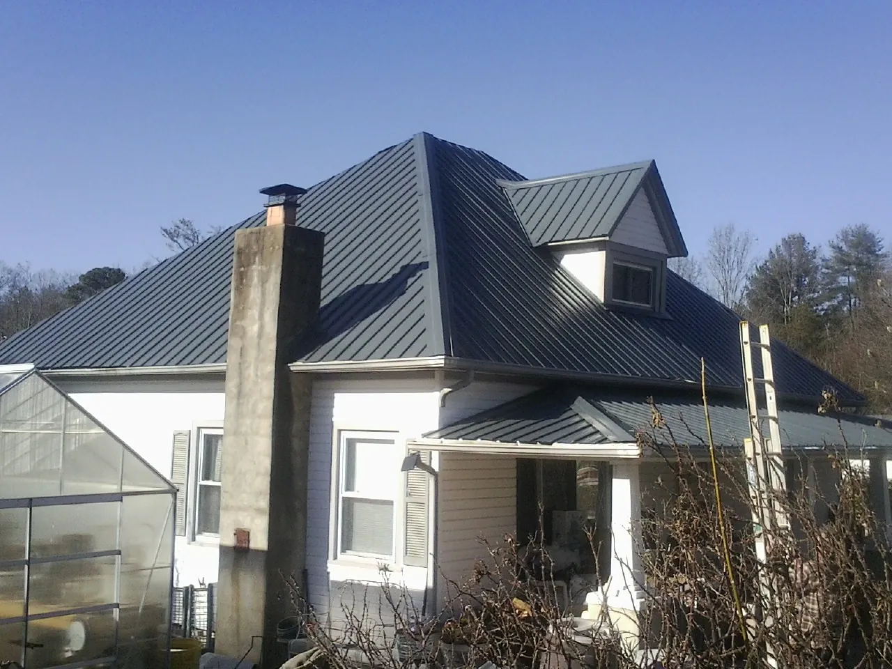 Dark blue standing seam metal roof on a white farmhouse with dormer — Slate & Tile Roof Repair by Roofing Brothers in Pond Eddy