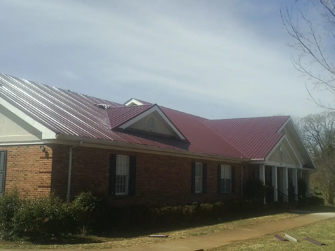 Red metal roof with gabled entries on a long brick building, from a Hail Damage Roof Repair job in Pond Eddy