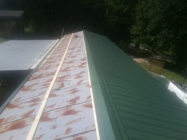 Old rusted panels beside newly installed green metal roofing — Wind Damage Roof Repair by Roofing Brothers in Pond Eddy