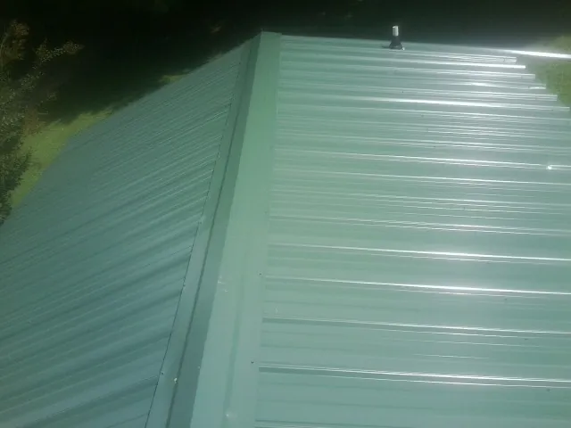 New green metal panels meeting at the ridge of a roof — Flat Roof Repair work by our crew in Pond Eddy