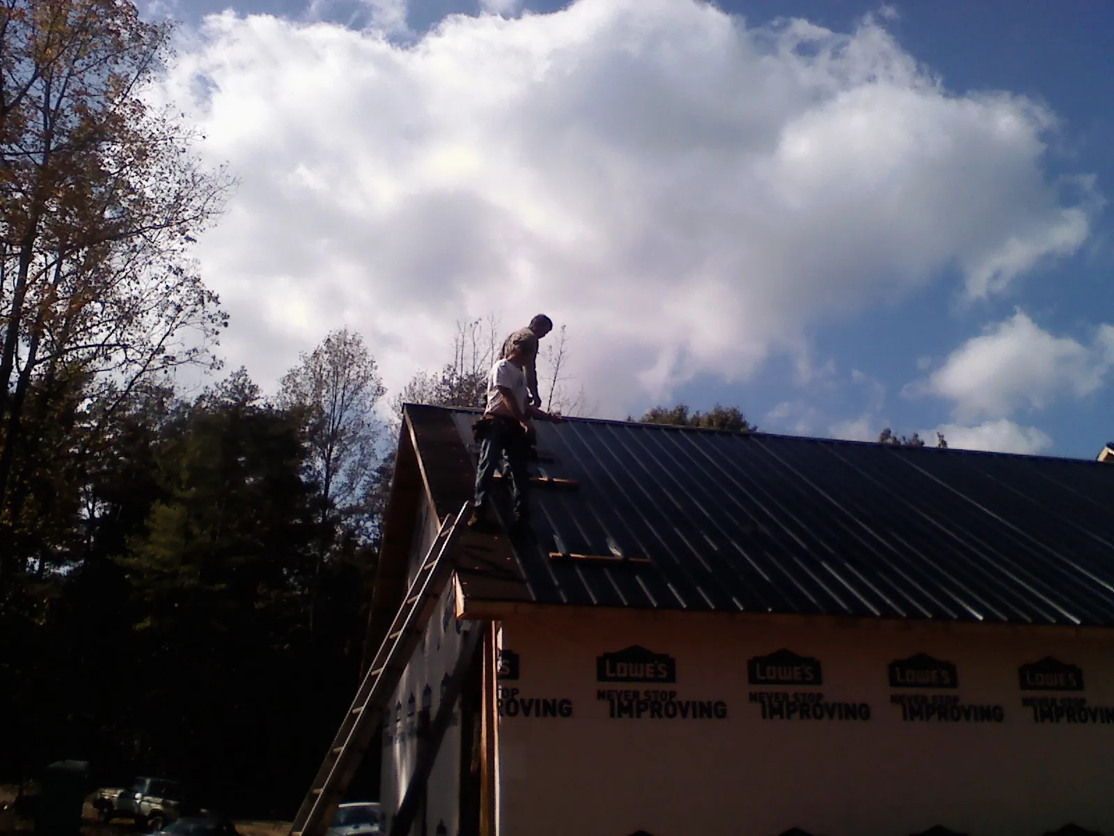 Roofer fastening dark metal panels high against a cloudy sky, from a Roof Inspection job in Pond Eddy