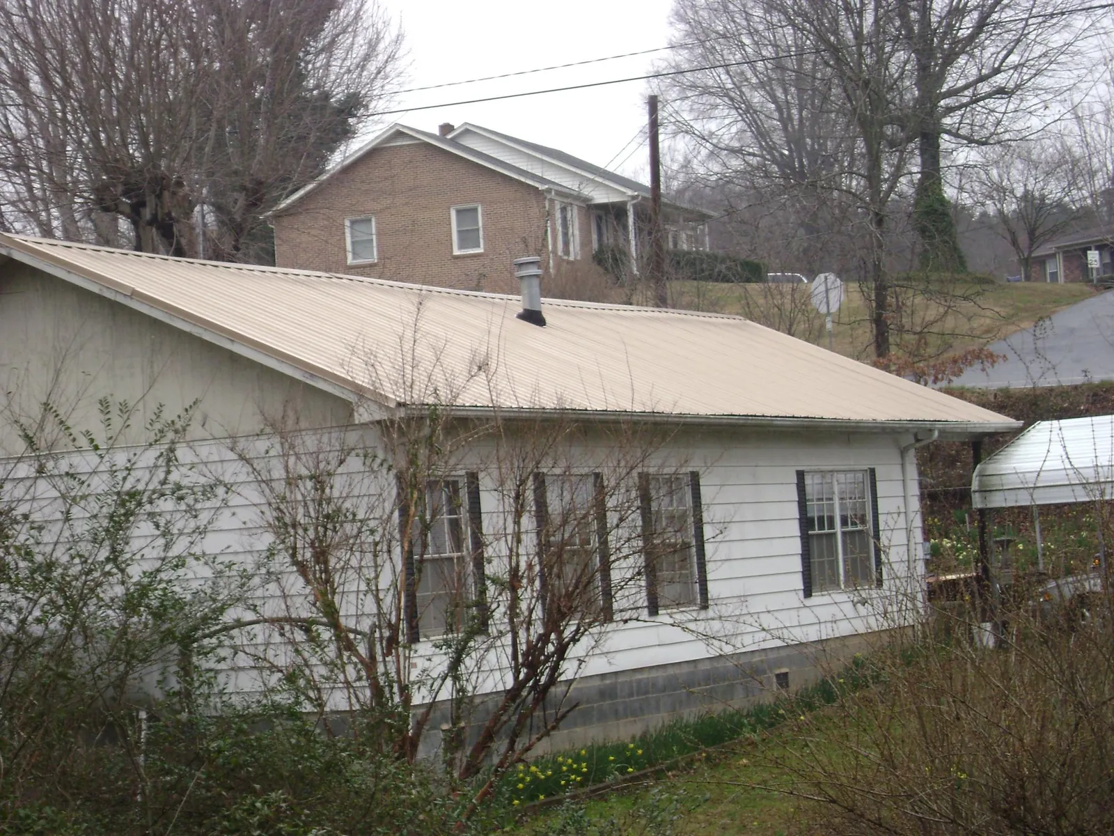 Tan metal roof on a white sided house set into a hillside — Commercial Roofing by Roofing Brothers in Pond Eddy
